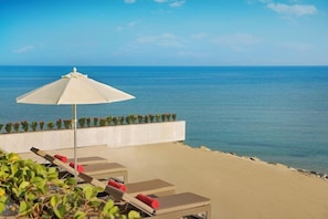 A beachside lounge area with sun loungers and a large umbrella, overlooking the sea.