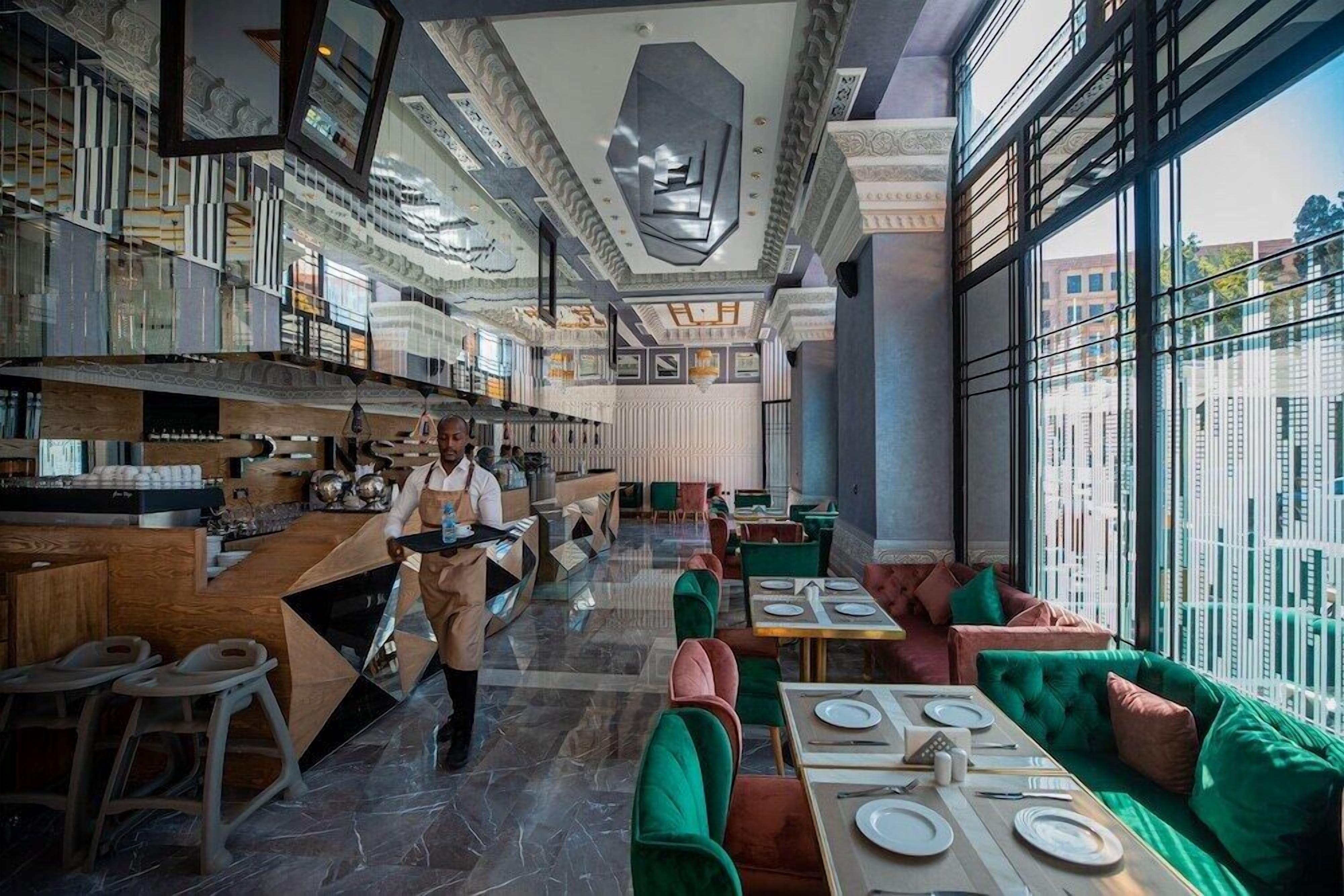 A modern restaurant interior with a bar area, seating, and a view through large windows.