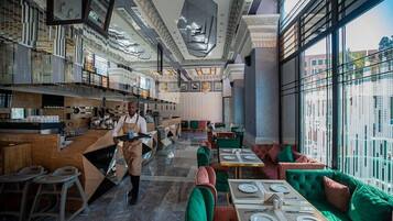 A modern restaurant interior with a bar area, seating, and a view through large windows.