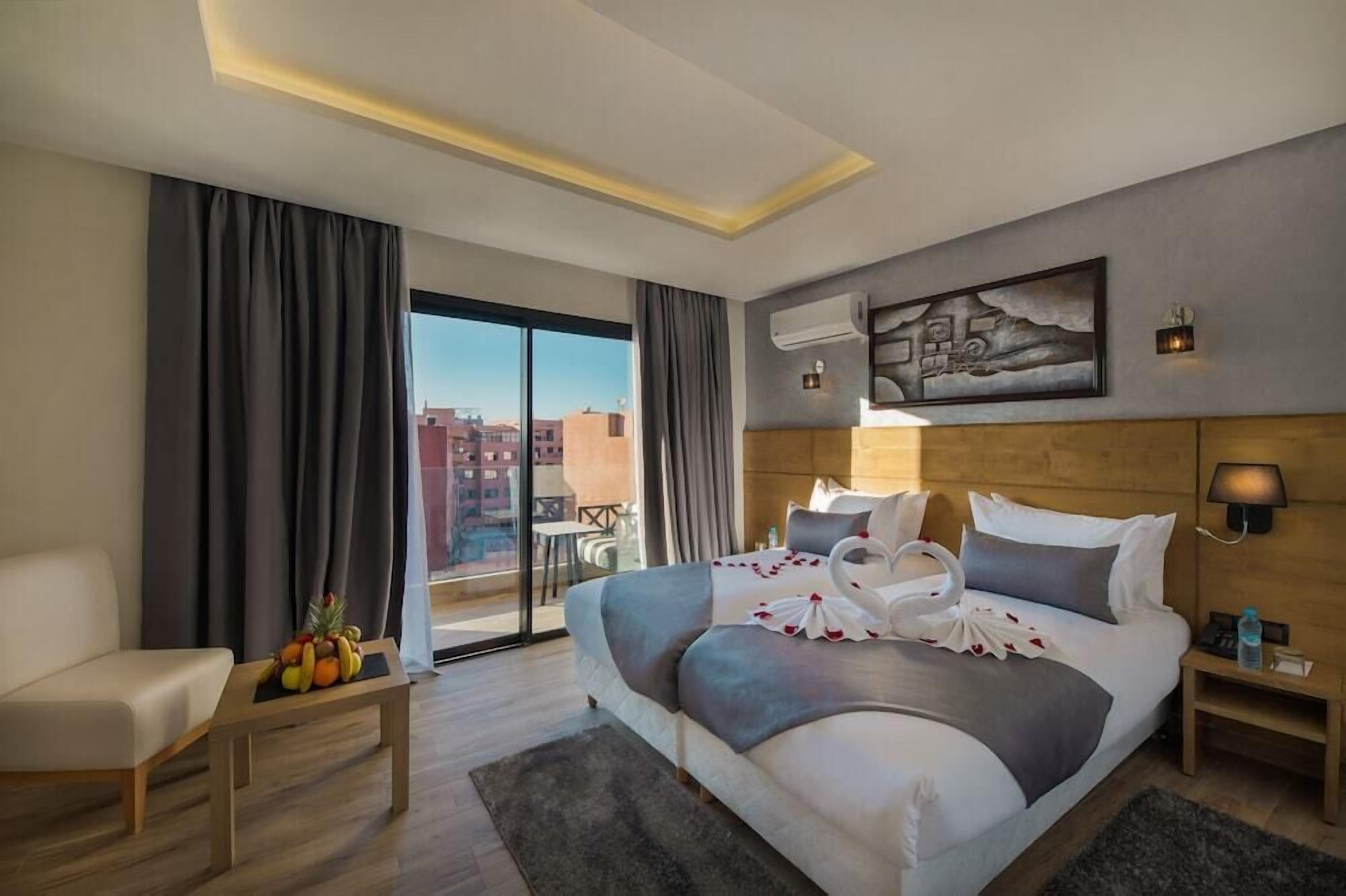 A hotel room with a bed, a sofa, a table with fruit, a balcony, and a city view.