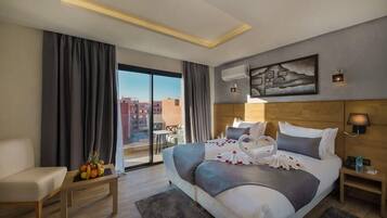 A hotel room with a bed, a sofa, a table with fruit, a balcony, and a city view.