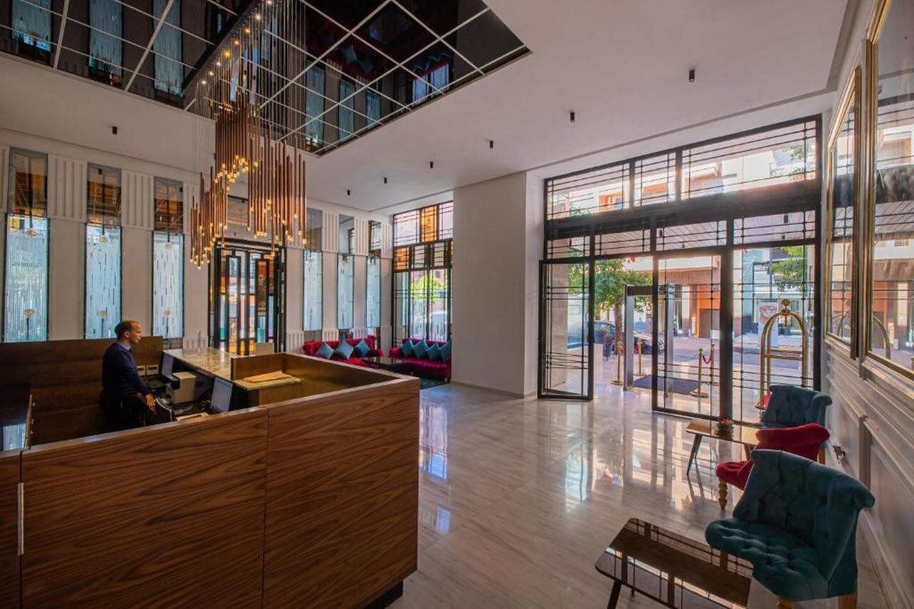 Eine moderne Hotellobby mit Empfangstresen, einer Sitzgelegenheit und großen Fenstern mit Blick auf die Straße.