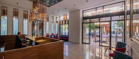 Una moderna hall d'albergo con reception, area salotto e ampie finestre che danno sulla strada.