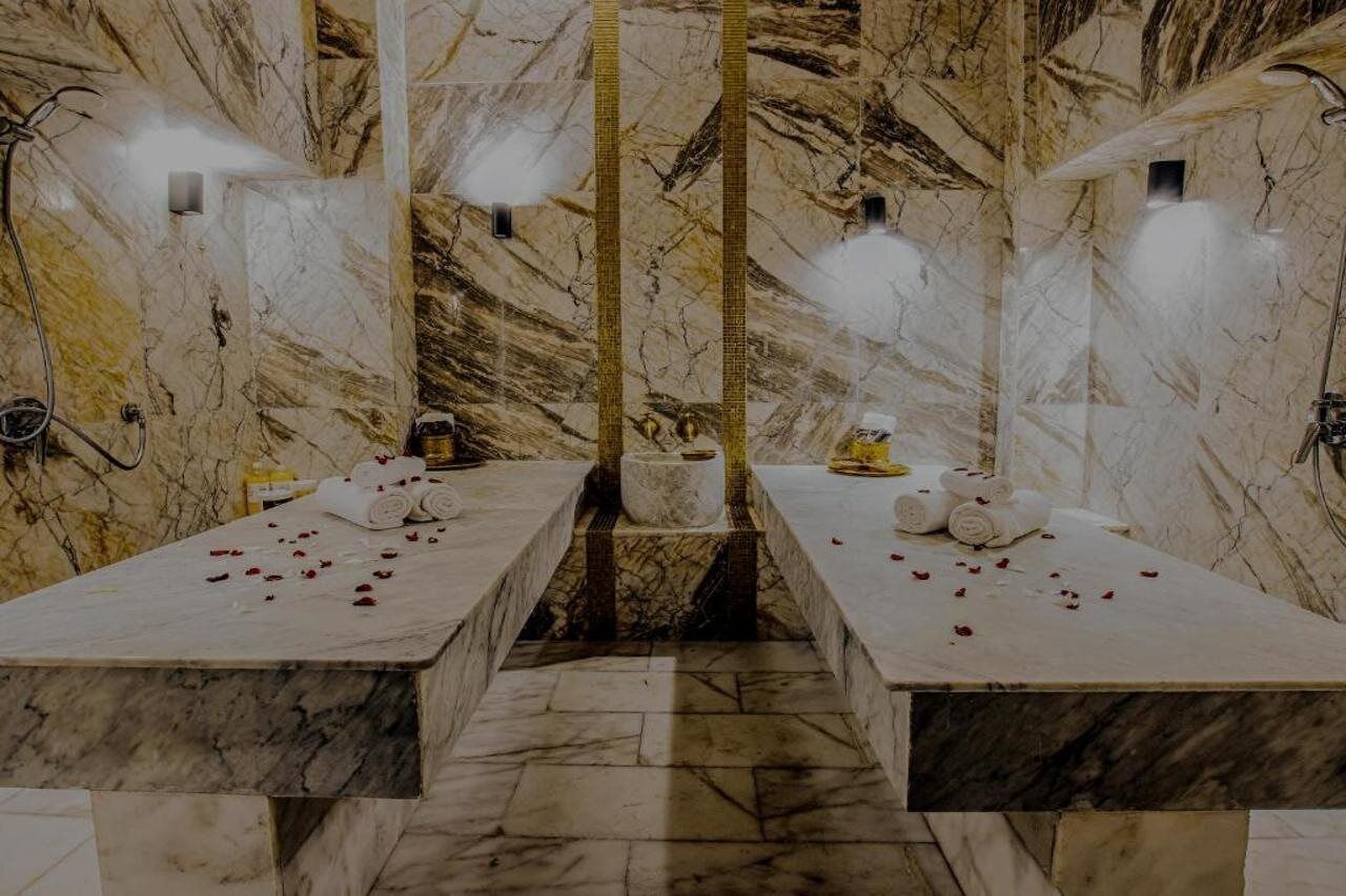 Ein Spa mit Marmorböden und zwei Behandlungsplätzen, jeweils mit Handtüchern und Rosenblüten.