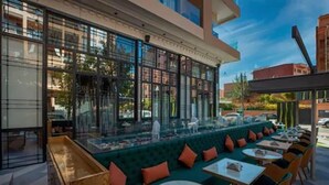 An outdoor seating area with tables and chairs, a green cushioned bench, and a glass enclosure with a view of the street. - Stars Hotel and Spa (Marrakech)