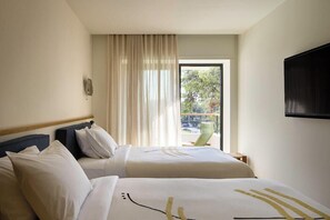 A hotel room with two beds, a large window with curtains, a flat-screen TV mounted on the wall, and a balcony with a chair. - Fenix Hotel (Glyfada)