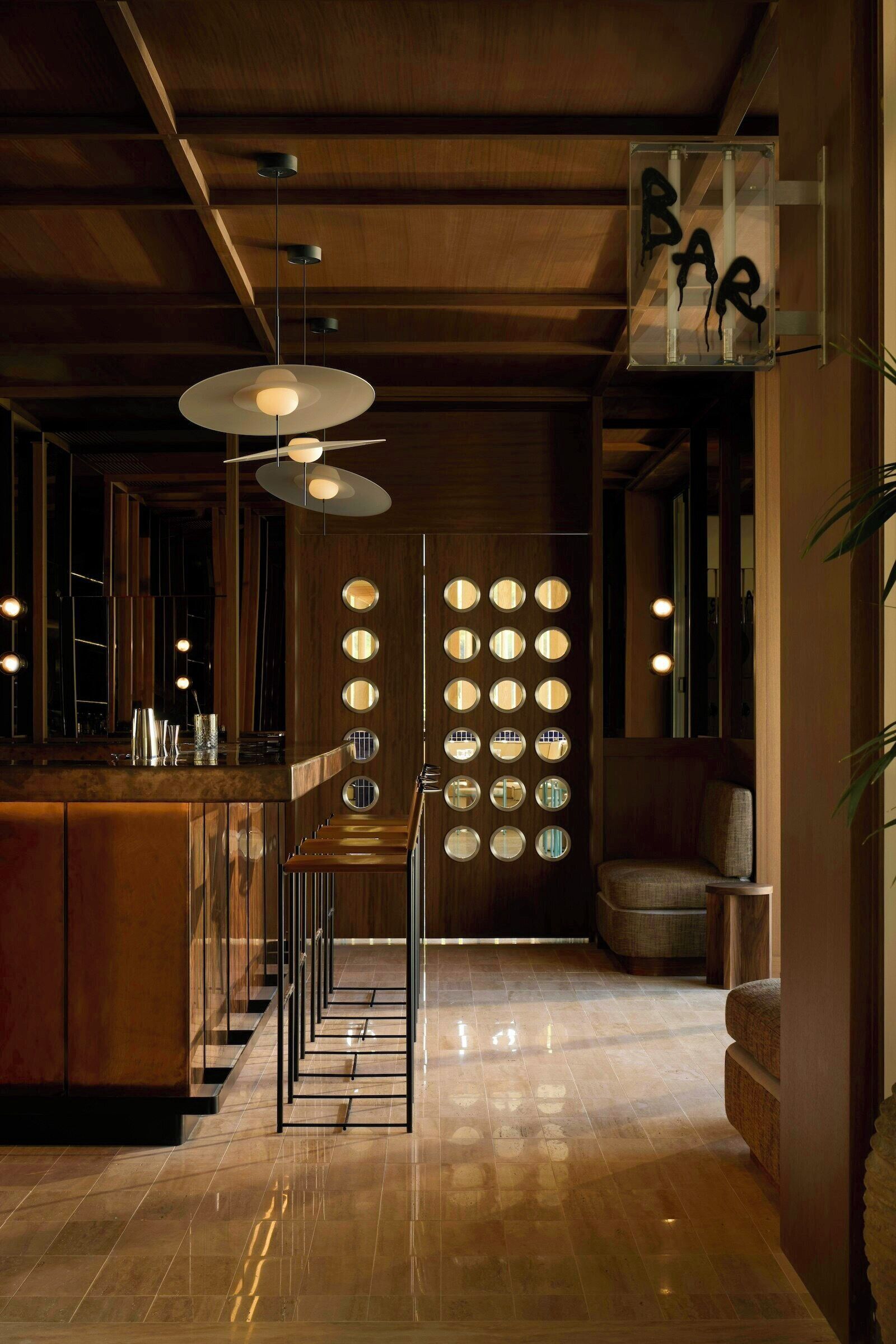 A bar area with a wooden ceiling, hanging pendant lights, and a wall with circular mirrors.