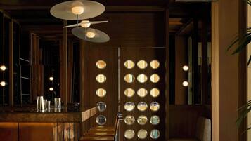 A bar area with a wooden ceiling, hanging pendant lights, and a wall with circular mirrors.