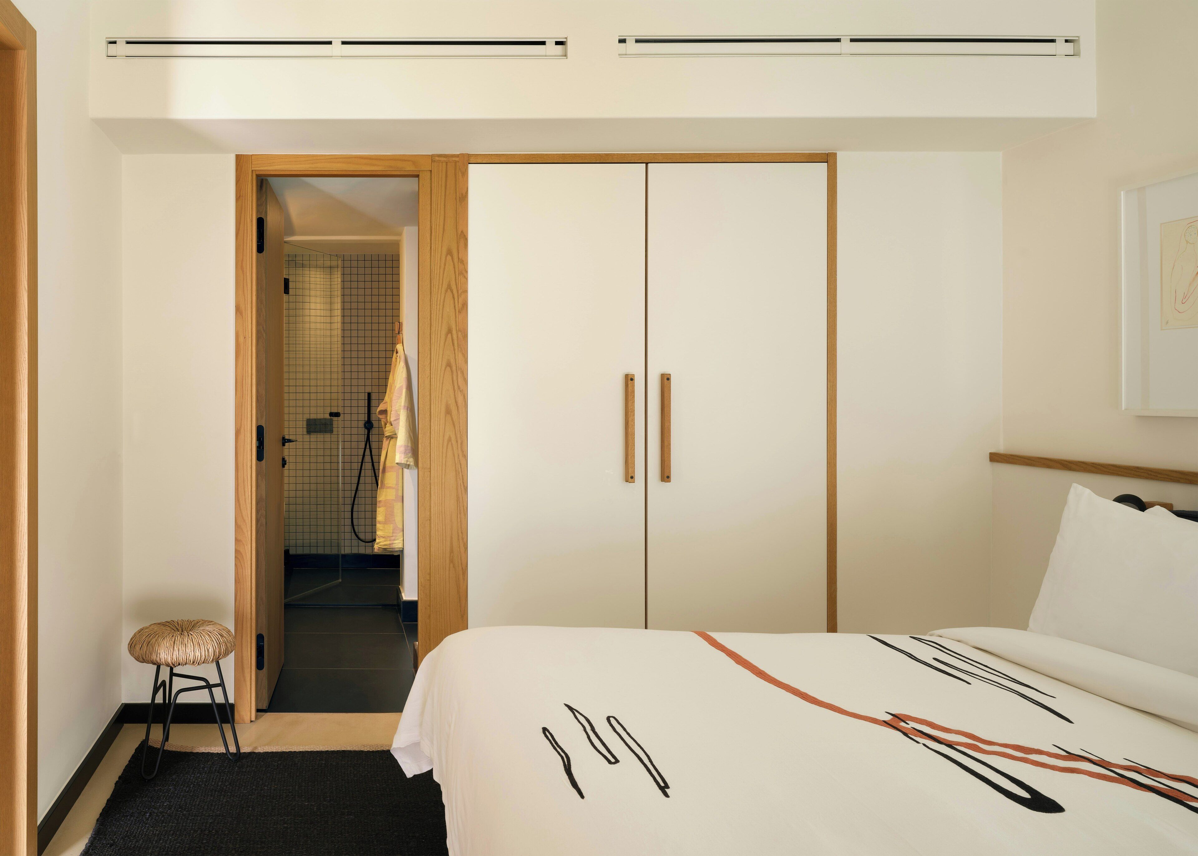 A hotel room with a bed, a wardrobe, a small stool, and a shower area.