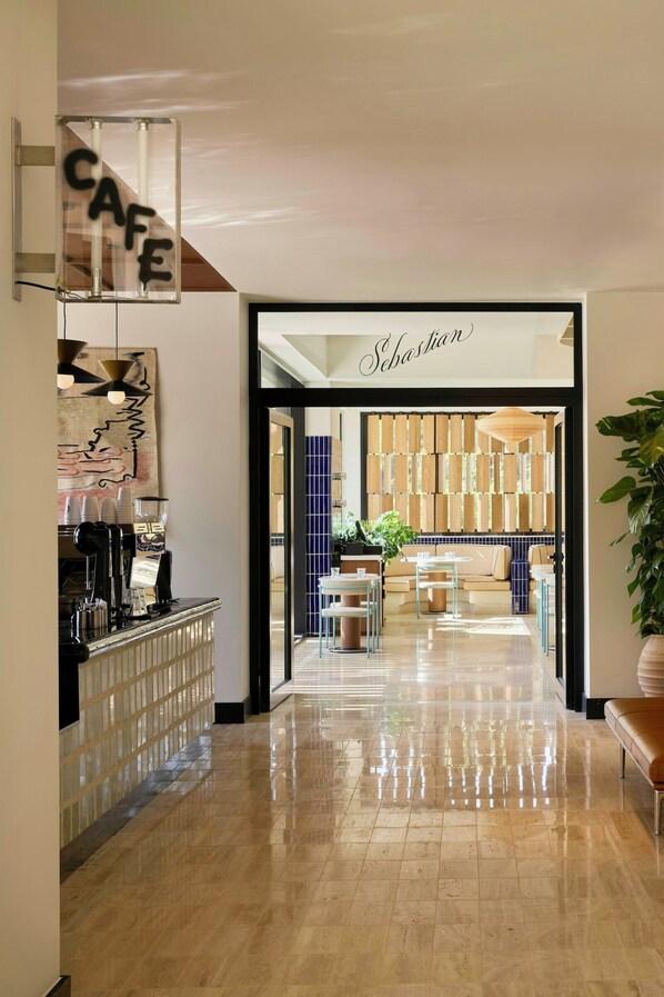 A modern interior with a cafe sign, a reception desk, and a seating area with a sofa and tables. - Fenix Hotel (Glyfada)