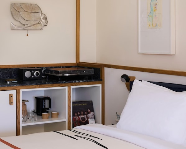 A hotel room with a bed, a desk with a radio, a coffee maker, and a shelf with a poster. - Fenix Hotel (Glyfada)