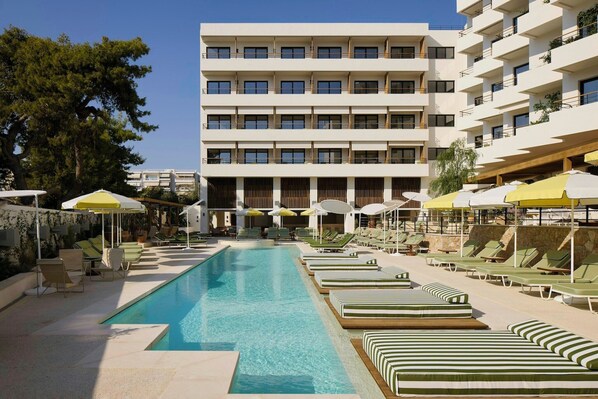 A swimming pool with lounge chairs and umbrellas, a multi-story building with balconies, and a clear sky. - Fenix Hotel (Glyfada)