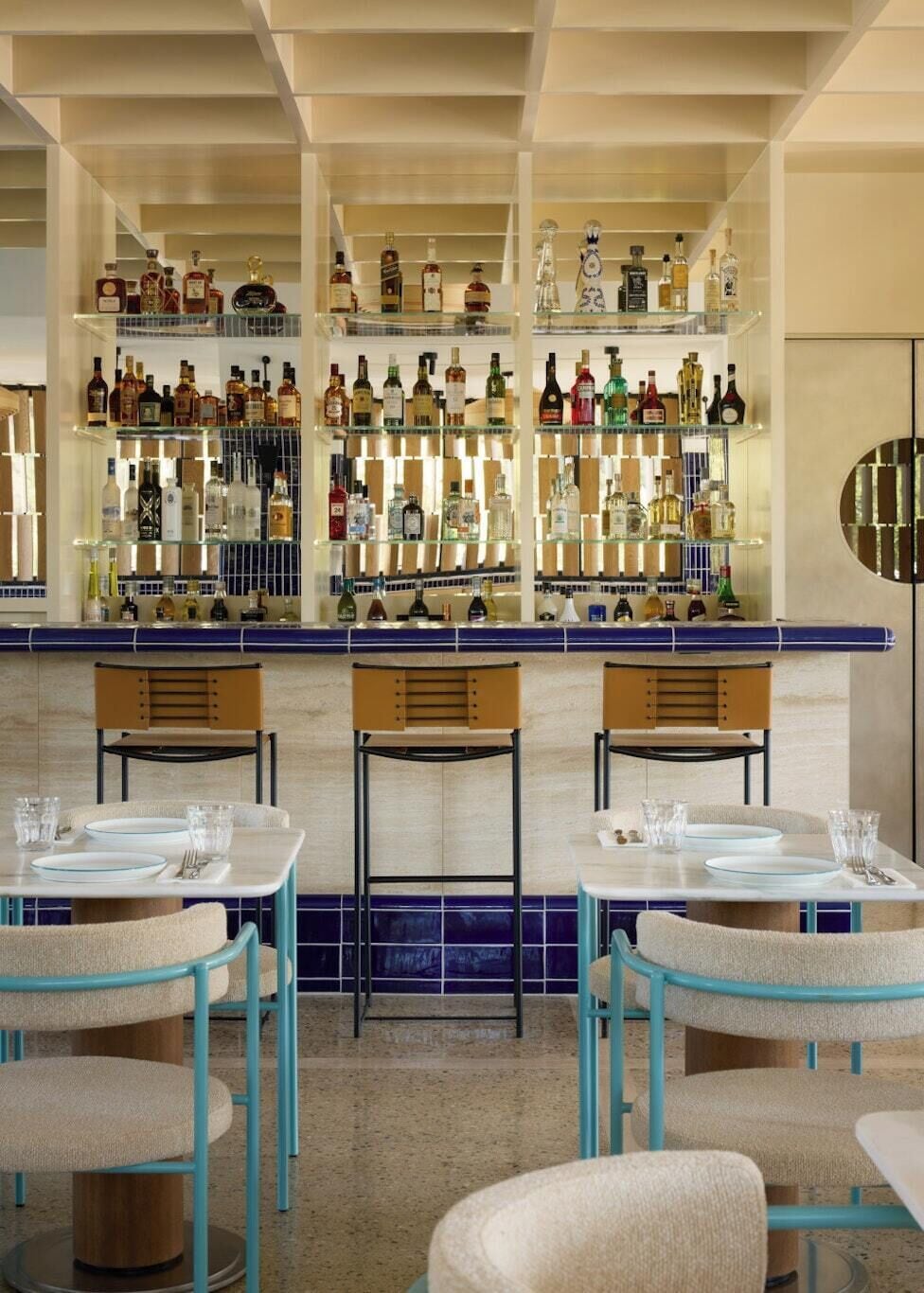 A bar area with multiple shelves of liquor bottles, bar stools, and tables set for dining.