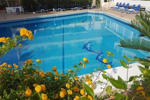 A swimming pool with clear blue water, surrounded by lounge chairs and yellow flowers. - Fenix Hotel (Glyfada)