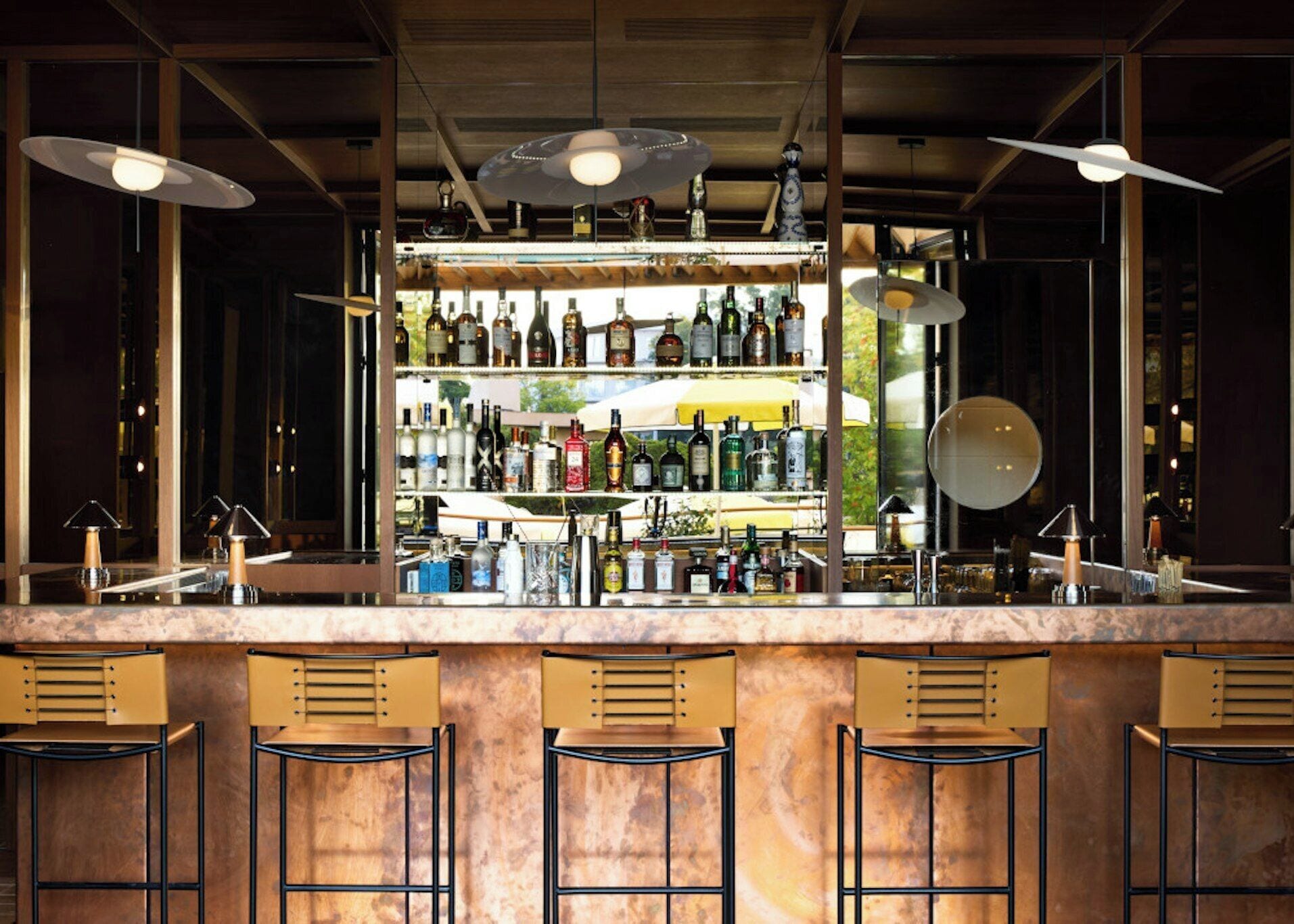 Een bar met een marmeren aanrecht, meerdere barkrukken en een verscheidenheid aan flessen op planken.