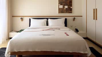 A neatly made bed with a white bedspread, a bedside table with a book and remote, and a wall-mounted artwork above the bed.