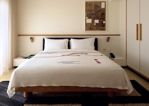 Ein ordentlich bezogenes Bett mit weißer Bettdecke, ein Nachttisch mit Buch und Fernbedienung und ein Wandbild über dem Bett.