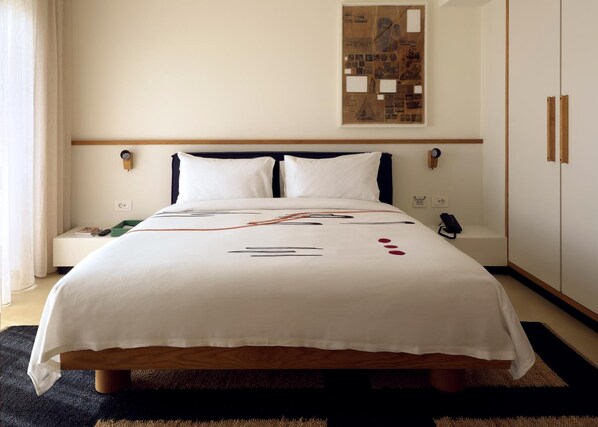 A neatly made bed with a white bedspread, a bedside table with a book and remote, and a wall-mounted artwork above the bed. - Fenix Hotel (Glyfada)