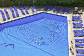 A swimming pool with a person swimming, surrounded by blue lounge chairs. - Fenix Hotel (Glyfada)