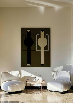 A modern room with two white armchairs, a coffee table, and a wall-mounted abstract painting. - Fenix Hotel (Glyfada)