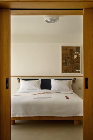 A bed with a white bedspread, wooden headboard, and a wall-mounted artwork. - Fenix Hotel (Glyfada)