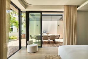 Une chambre d’hôtel moderne dotée d’un grand lit, d’un coin repas avec une table et des chaises, et d’une porte-fenêtre coulissante donnant sur un balcon agrémenté de plantes.