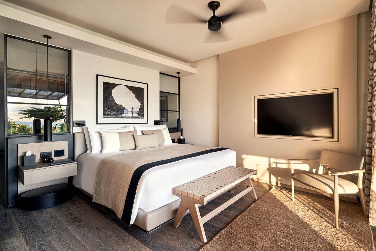 A modern bedroom with a bed, bedside tables, a bench, a TV, and a large window.