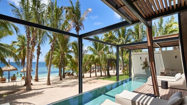 A glass-enclosed infinity pool with a beach view, lounge chairs, and a wooden deck.