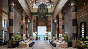 A spacious lobby with a central pathway leading to a large window overlooking the sea, flanked by seating areas and a bar.