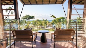 A covered outdoor seating area with wicker furniture, a round table, and a view of the ocean and palm trees.