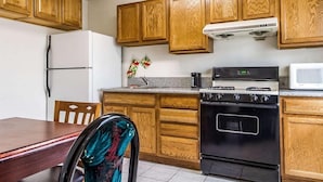 A kitchen with wooden cabinets, a white refrigerator, a stove, and a microwave. - Rodeway Inn Auburn, CA (Auburn)