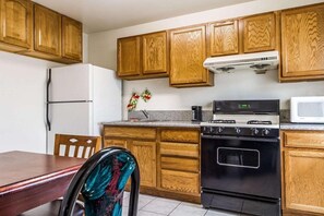 Eine Küche mit Holzschränken, einem weißen Kühlschrank, einem Herd und einer Mikrowelle.