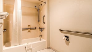A bathroom with a bathtub, shower, grab bars, and a toilet. - Rodeway Inn Auburn, CA (Auburn)