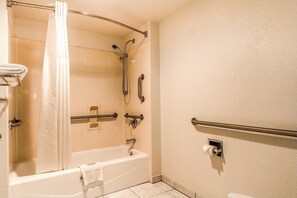 Ein Badezimmer mit Badewanne, Dusche, Haltegriffen und Toilette.