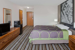 Una habitación de hotel con cama, televisión, microondas, cómoda y puerta.