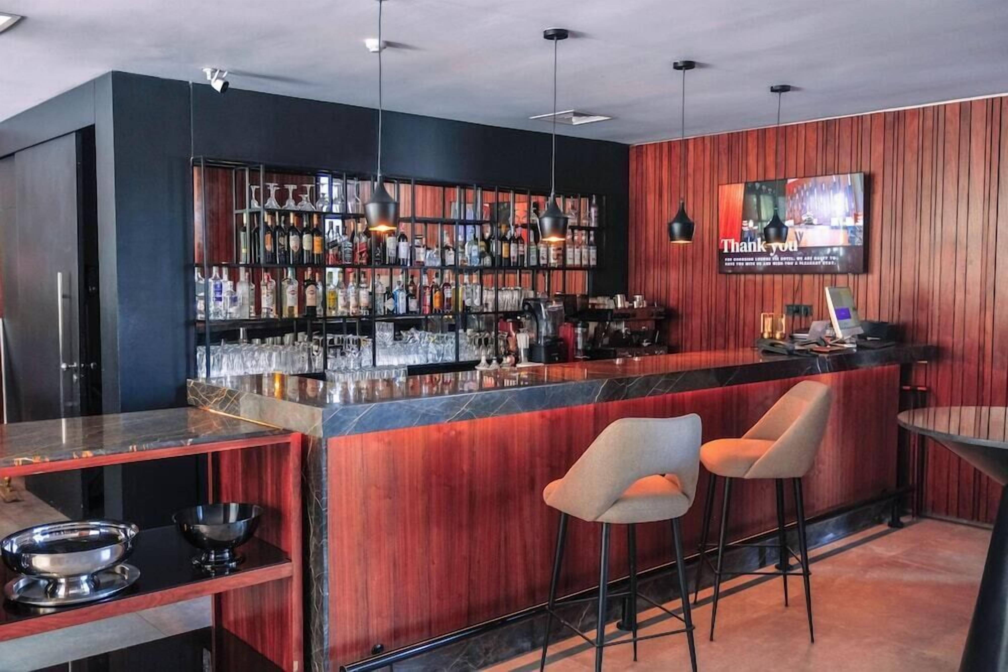 A bar area with a wooden wall, a TV screen, and a bar counter with stools.
