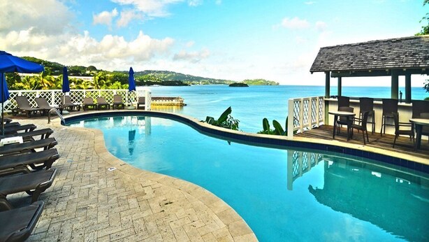 A swimming pool with lounge chairs and a covered seating area, surrounded by a white fence and a view of the sea. - Secrets St. Lucia Resort & Spa Adults Only (Gros Islet)