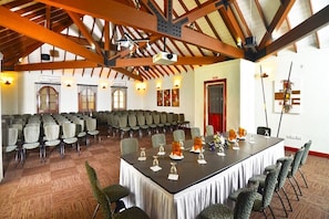 Un salón de conferencias con una larga mesa, varias sillas y un techo alto con vigas a la vista.