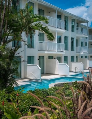 Un hotel de varios pisos con balcones, piscina y abundante vegetación.