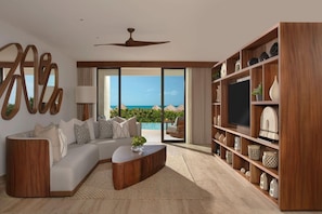 A modern living room with a curved sofa, a coffee table, and a large TV on a wooden shelf. - Secrets Playa Blanca Costa Mujeres (Costa Mujeres)