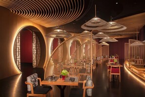 Interior de restaurante com mobiliário de madeira, luminárias pendentes e design de parede curva.