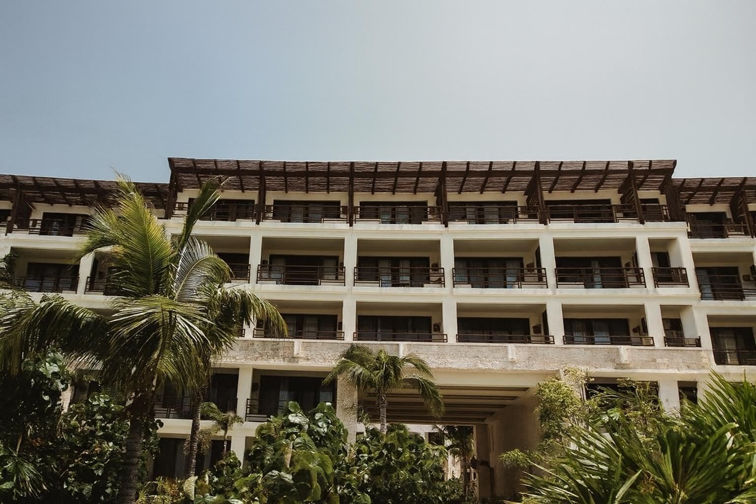 A multi-story hotel with balconies, surrounded by tropical vegetation.