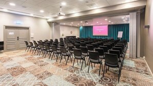 Ett konferensrum med rader av stolar, en projektorduk och en turkosfärgad bakgrundsridå.