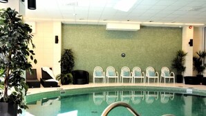 En inomhuspool med ett kaklat golv, en metallstege och flera vita stolar som är placerade längs en grön vägg.