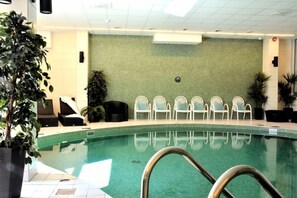 An indoor swimming pool with a tiled floor, a metal pool ladder, and several white chairs arranged against a green wall. - Quality Hotel Winn (Hisings Backa)