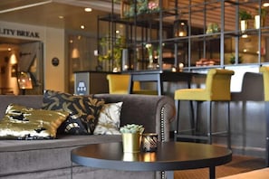 A modern lounge area with a sofa, a round table, and a bar area with chairs. - Quality Hotel Winn (Hisings Backa)