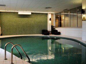 Una piscina interior con pared verde, un cartel de seguridad y una ventana con persianas.