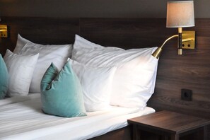 A neatly made bed with white and teal pillows, a wooden headboard, and a wall-mounted lamp. - Quality Hotel Winn (Hisings Backa)