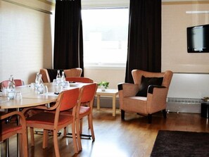 A hotel room with a dining table, chairs, a small side table, a sofa, a TV mounted on the wall, and a window with curtains. - Quality Hotel Winn (Hisings Backa)