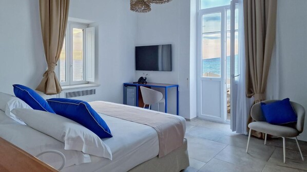 Une chambre d’hôtel avec un lit, un bureau, une chaise, une télévision et une vue sur la mer.